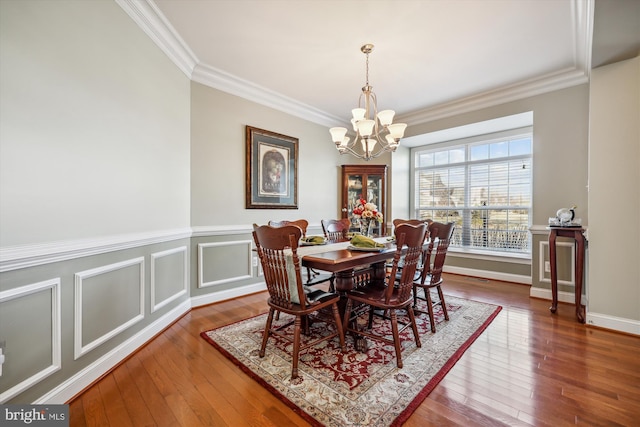 dining space featuring hardwood / wood-style flooring, ornamental molding, a decorative wall, and a notable chandelier