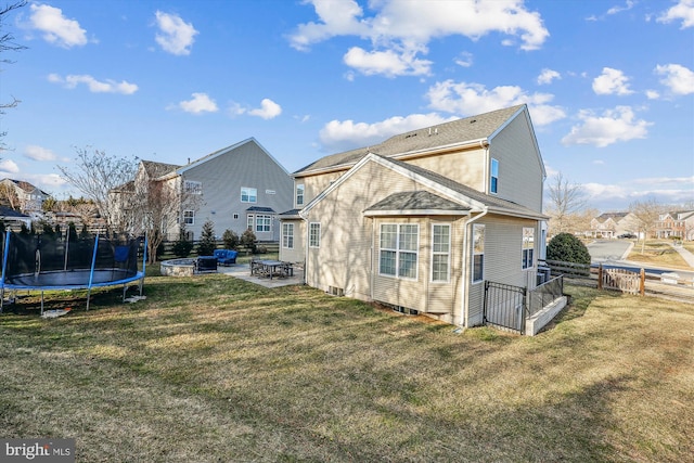 rear view of property featuring a trampoline, a patio area, fence, and a lawn