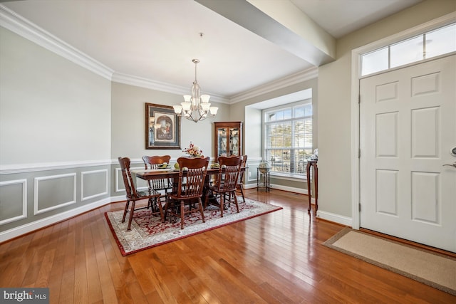 dining space featuring crown molding, a decorative wall, an inviting chandelier, and hardwood / wood-style flooring