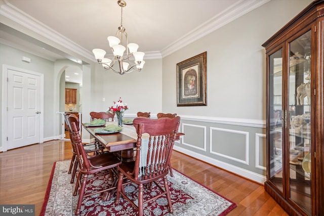 dining space featuring arched walkways, a decorative wall, an inviting chandelier, ornamental molding, and wood finished floors