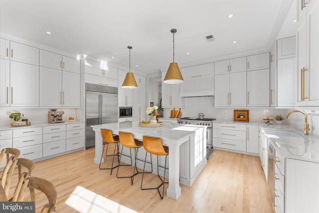 kitchen with a center island, light wood-style floors, a sink, built in appliances, and a kitchen breakfast bar