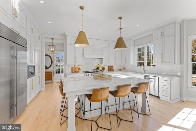 kitchen with a breakfast bar, white cabinets, light wood-style flooring, and built in appliances