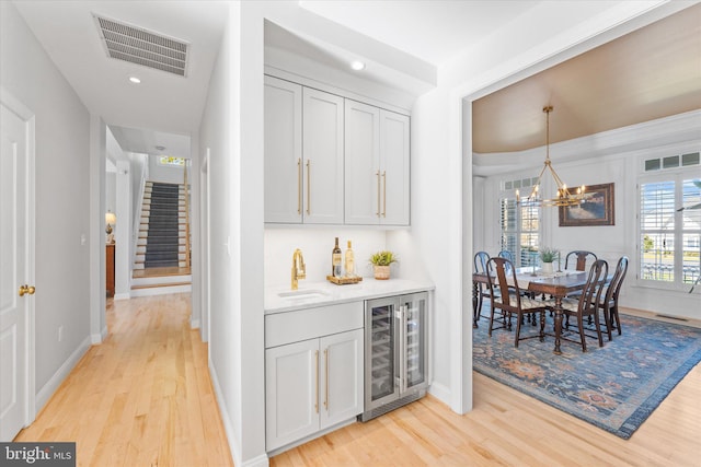 interior space featuring beverage cooler, a bar, light wood finished floors, and visible vents