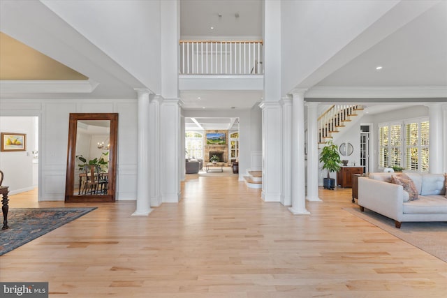 entryway featuring ornate columns, stairway, a decorative wall, and light wood-style floors