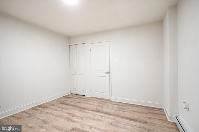 unfurnished bedroom with a baseboard heating unit, light wood-type flooring, a closet, and baseboards