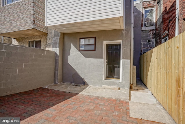 entrance to property featuring a patio area, fence, and stucco siding