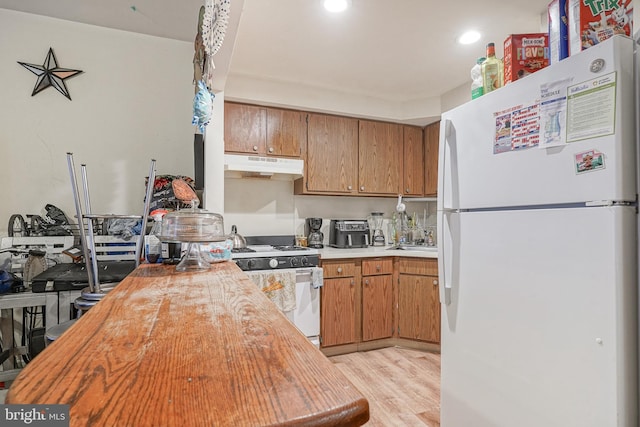 kitchen featuring white appliances, light wood finished floors, brown cabinets, light countertops, and under cabinet range hood