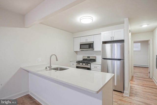 kitchen with a peninsula, baseboard heating, stainless steel appliances, light wood-style floors, and a sink