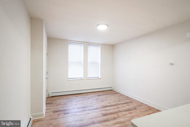 unfurnished room featuring a baseboard heating unit, wood finished floors, and baseboards