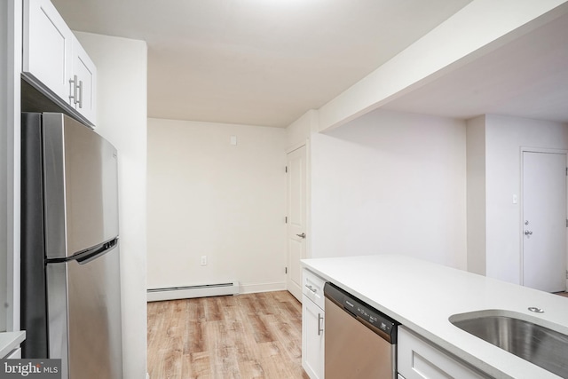 kitchen featuring stainless steel appliances, light countertops, a baseboard heating unit, white cabinets, and light wood-type flooring