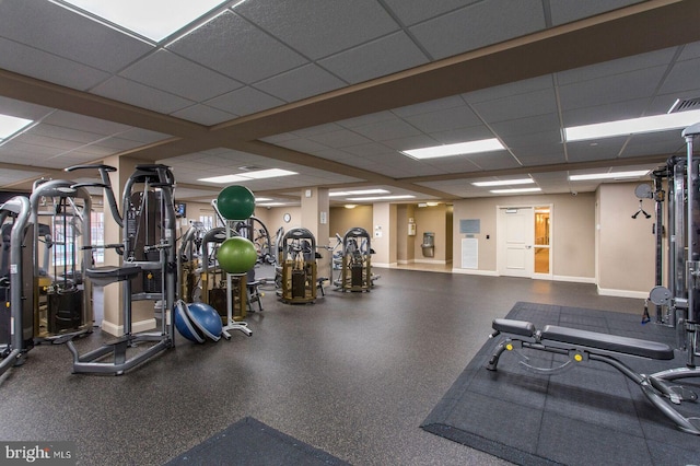 workout area featuring a paneled ceiling and baseboards