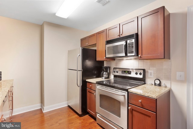 kitchen featuring visible vents, decorative backsplash, light stone counters, stainless steel appliances, and light wood-type flooring