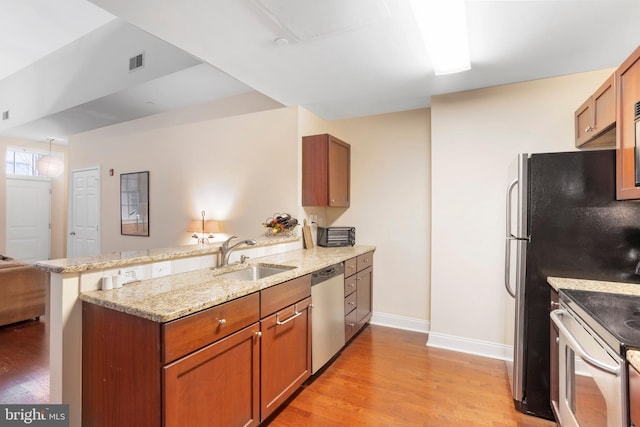 kitchen featuring a peninsula, a sink, stainless steel dishwasher, light wood-type flooring, and brown cabinets