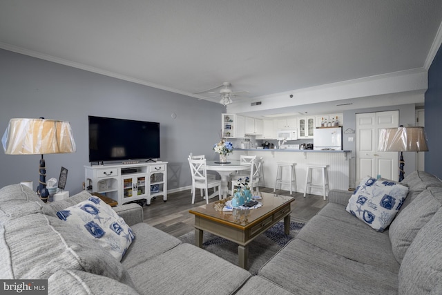 living area with baseboards, ceiling fan, ornamental molding, and dark wood-type flooring