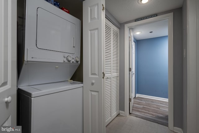 clothes washing area with laundry area, baseboards, visible vents, a textured ceiling, and stacked washing maching and dryer