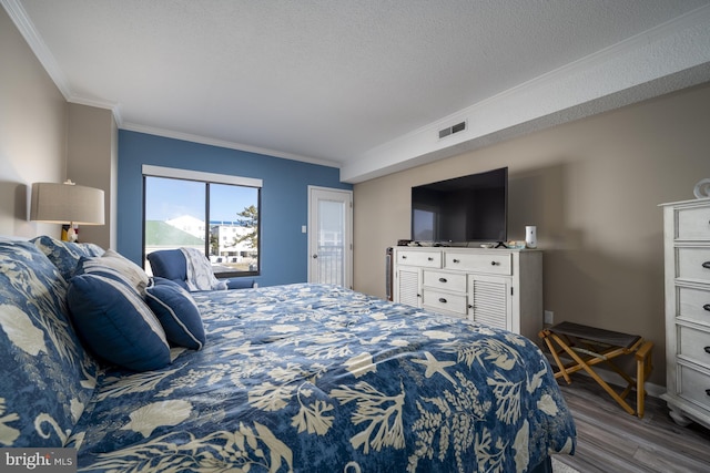 bedroom featuring a textured ceiling, ornamental molding, wood finished floors, and visible vents