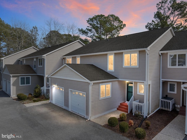 view of front facade featuring aphalt driveway, roof with shingles, an attached garage, and central AC unit