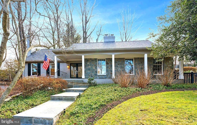 view of front facade with stone siding, covered porch, a chimney, and a front lawn