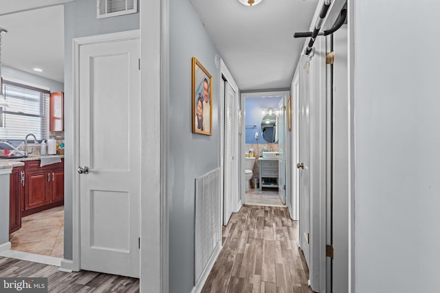 hall with visible vents, a sink, and light wood-style flooring