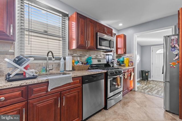 kitchen with reddish brown cabinets, light tile patterned floors, stainless steel appliances, backsplash, and a sink