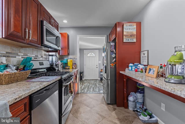 kitchen with light tile patterned flooring, stainless steel appliances, light stone countertops, reddish brown cabinets, and tasteful backsplash