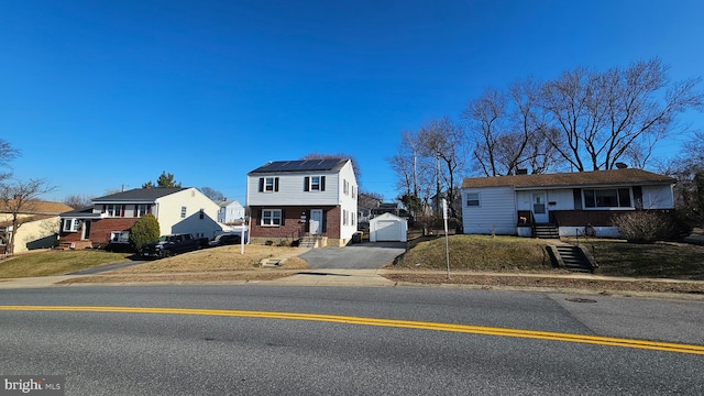 view of front of home with an outbuilding, aphalt driveway, brick siding, a residential view, and roof mounted solar panels