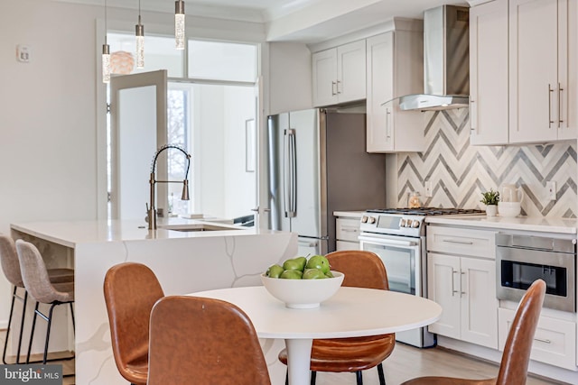 kitchen with a kitchen island with sink, a sink, appliances with stainless steel finishes, wall chimney range hood, and a kitchen bar