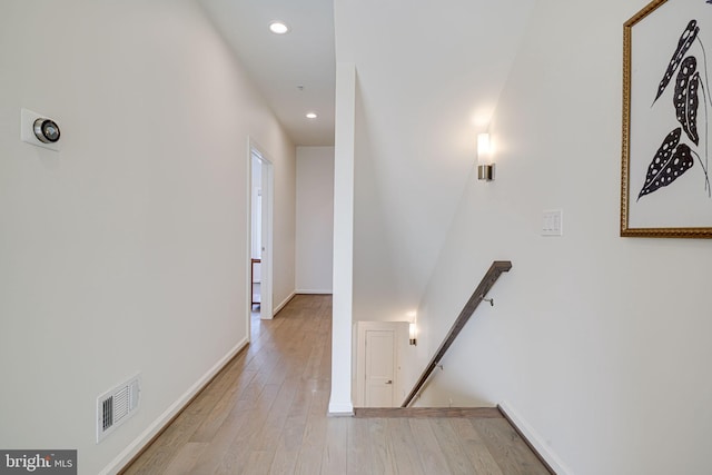 hallway featuring light wood-type flooring, baseboards, visible vents, and an upstairs landing