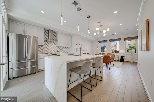 kitchen with a sink, visible vents, wall chimney range hood, light wood-type flooring, and freestanding refrigerator