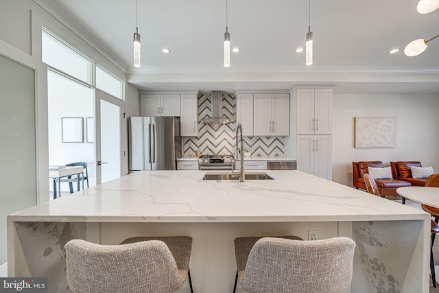 kitchen with tasteful backsplash, wall chimney exhaust hood, light stone counters, freestanding refrigerator, and a sink