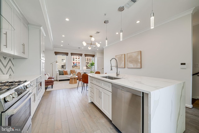 kitchen featuring a sink, open floor plan, appliances with stainless steel finishes, ornamental molding, and light wood finished floors