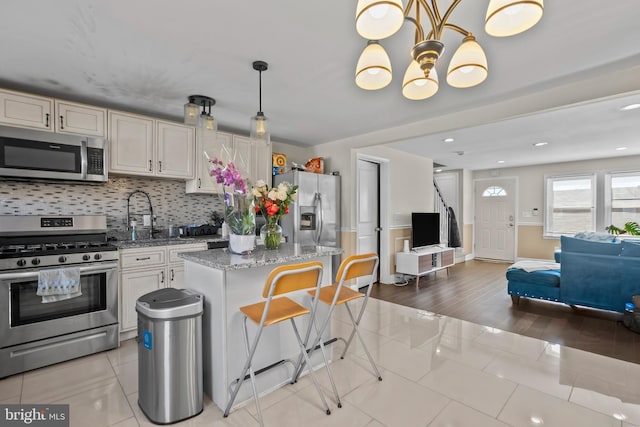 kitchen featuring backsplash, appliances with stainless steel finishes, open floor plan, a sink, and light stone countertops