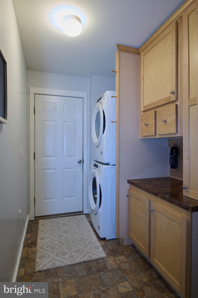 clothes washing area featuring stacked washer and clothes dryer, cabinet space, stone finish floor, and baseboards