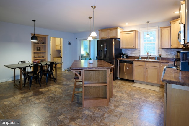 kitchen with stainless steel appliances, light brown cabinetry, dark countertops, and a center island