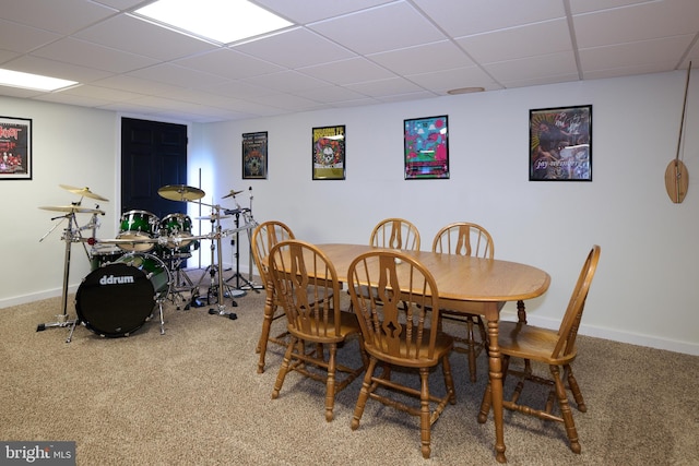 carpeted dining area with a paneled ceiling and baseboards