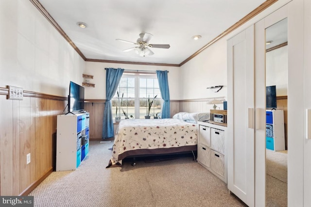 carpeted bedroom featuring a wainscoted wall, wooden walls, ceiling fan, and crown molding