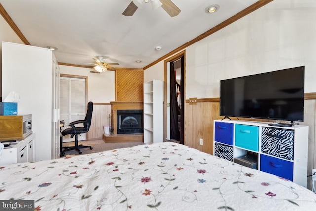 bedroom featuring a fireplace with raised hearth, ornamental molding, a wainscoted wall, and wooden walls