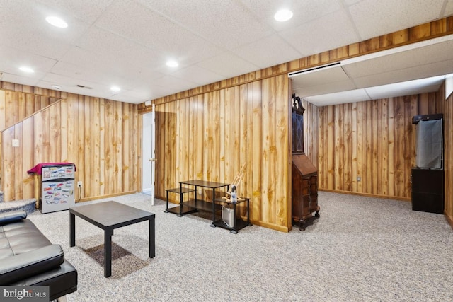 carpeted living room featuring wood walls, baseboards, a drop ceiling, and recessed lighting