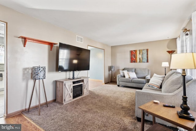 carpeted living area featuring visible vents, baseboards, and wood finished floors