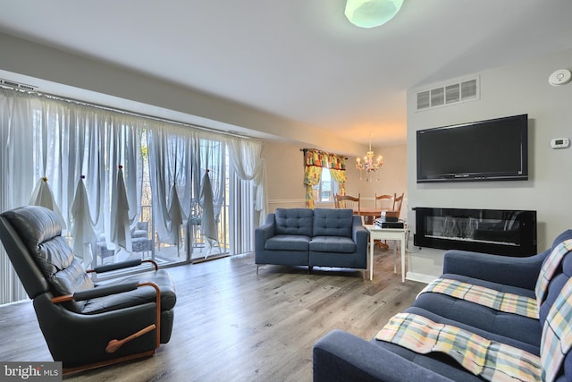 living room featuring a chandelier, visible vents, a glass covered fireplace, and wood finished floors