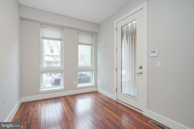 doorway with a healthy amount of sunlight, dark wood finished floors, visible vents, and baseboards