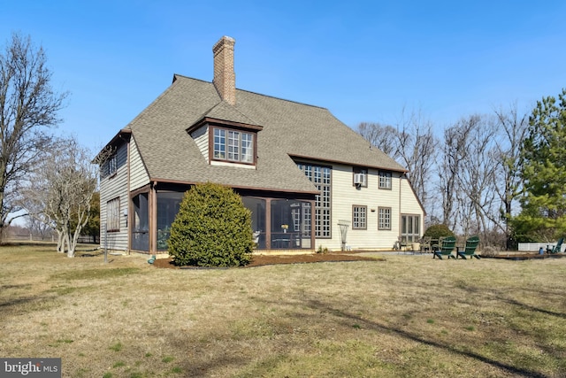 back of house with roof with shingles, a lawn, and a chimney