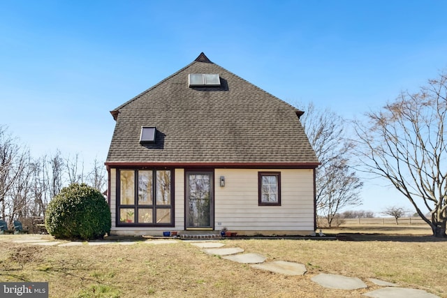 back of property with roof with shingles and a lawn