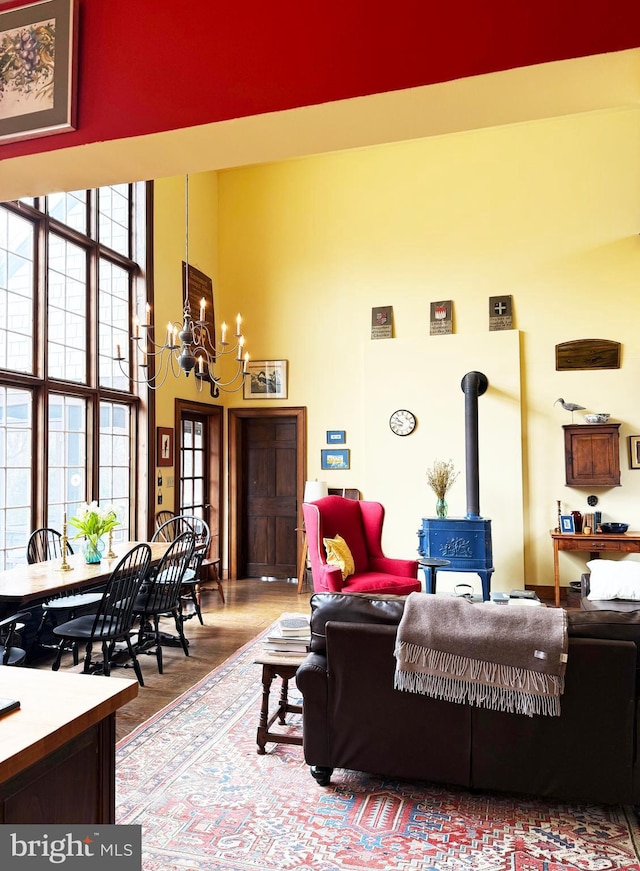 living area with a wood stove, a notable chandelier, a towering ceiling, and wood finished floors