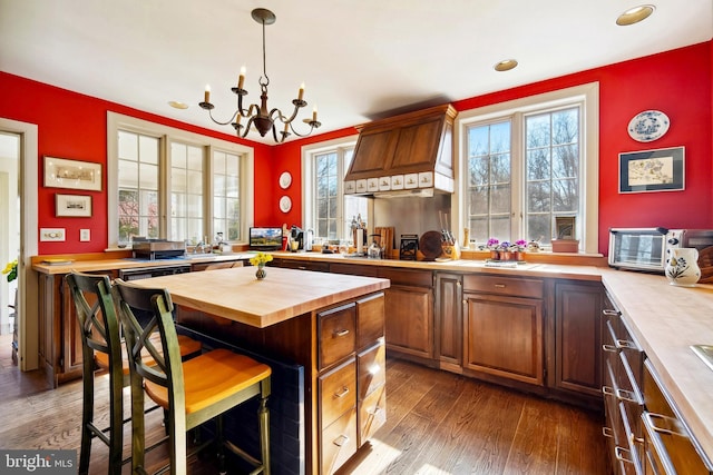 kitchen featuring a notable chandelier, a kitchen breakfast bar, wooden counters, dark wood finished floors, and custom range hood