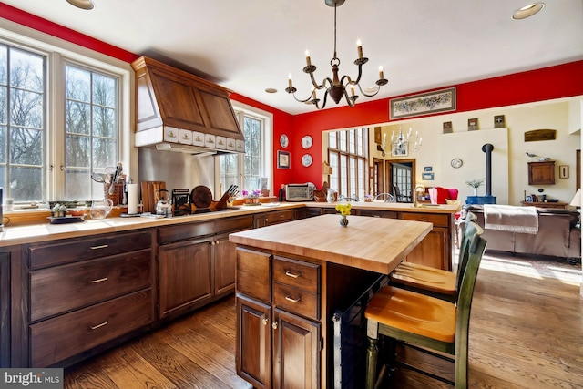 kitchen with dark wood-style floors, butcher block countertops, a peninsula, black electric cooktop, and premium range hood