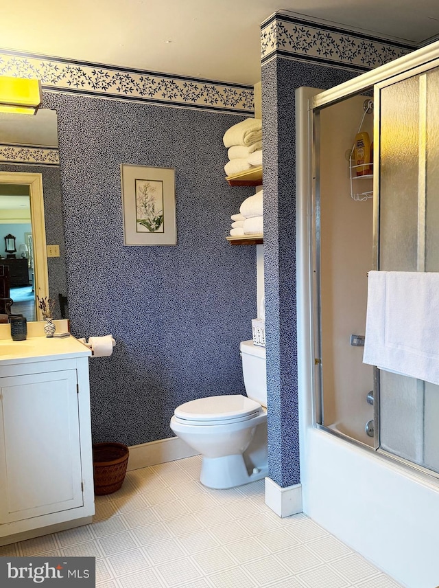 bathroom featuring toilet, shower / bath combination with glass door, vanity, baseboards, and wallpapered walls