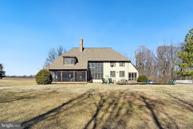 rear view of house with a sunroom, a yard, and a chimney