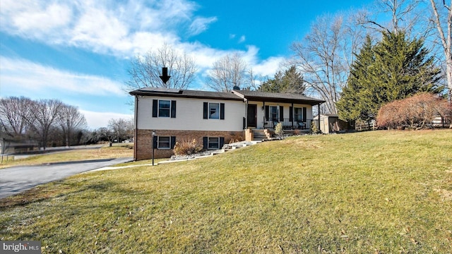 view of front of property featuring brick siding, covered porch, aphalt driveway, and a front yard