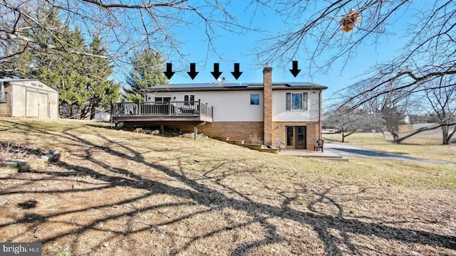 back of house featuring a storage unit, a deck, roof mounted solar panels, an outdoor structure, and brick siding